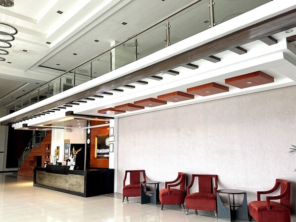 Un vestíbulo moderno con una mesa de recepción, sillas rojas y una escalera.