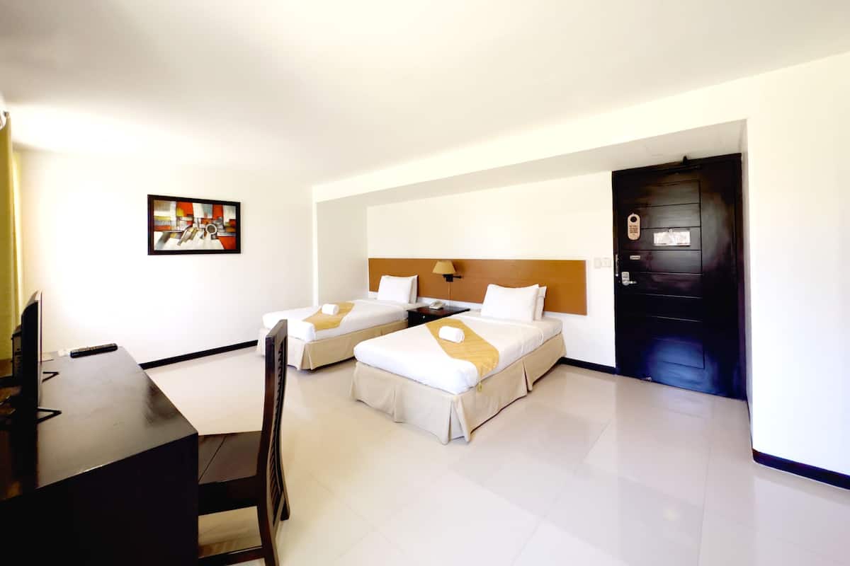 A hotel room with two beds, a desk, a chair, a painting on the wall, and a door.