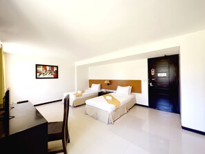 Habitación de hotel con dos camas, un escritorio, una silla, un cuadro en la pared y una puerta.