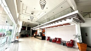 Un vestíbulo amplio con techo alto, luminarias modernas y una zona de estar con sillas rojas.