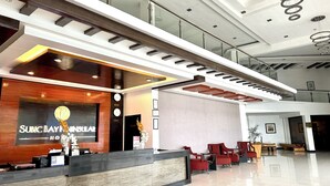 Zona de recepción de un hotel con diseño moderno, que incluye un mostrador de recepción, un área de descanso y una escalera que conduce a un nivel superior.