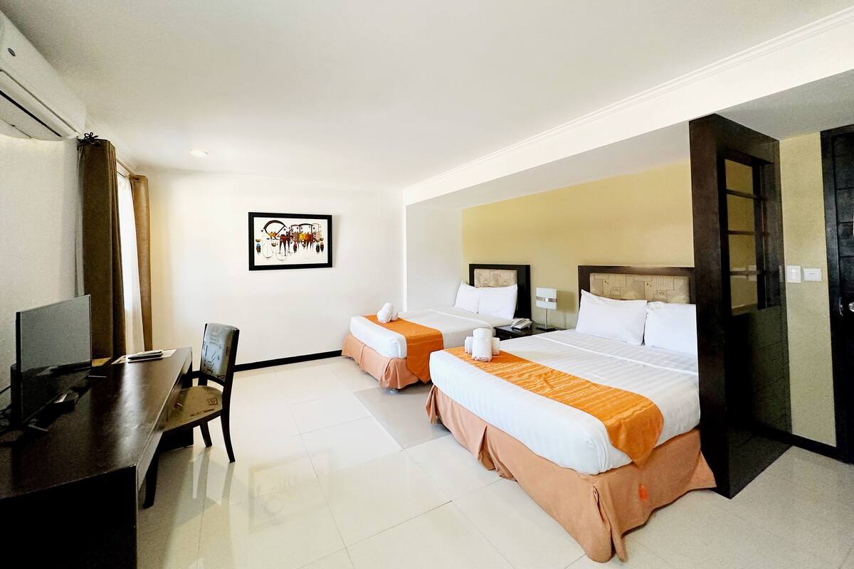 A hotel room with two beds, a desk, a chair, and a television.