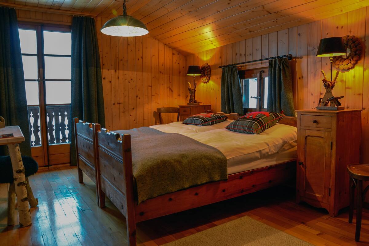 A wooden cabin bedroom with a bed, bedside tables, a desk, and a chair.
