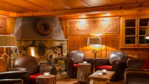 A cozy, wood-paneled room with leather chairs, a stone fireplace, and a wooden wall with a carved design. - Hotel Le Grand Chalet Favre (Anniviers)