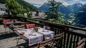 An outdoor dining area with tables set for two, overlooking a mountainous landscape. - Hotel Le Grand Chalet Favre (Anniviers)