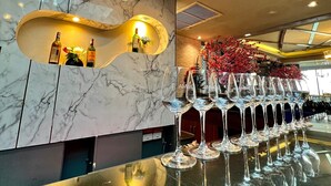 Zona de bar moderna con pared de mármol, exposición de copas de vino y tragaluz en el techo.