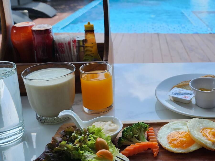 A breakfast tray with eggs, sausages, toast, and a side salad, along with two glasses of milk and orange juice, and condiments on a table by a pool.