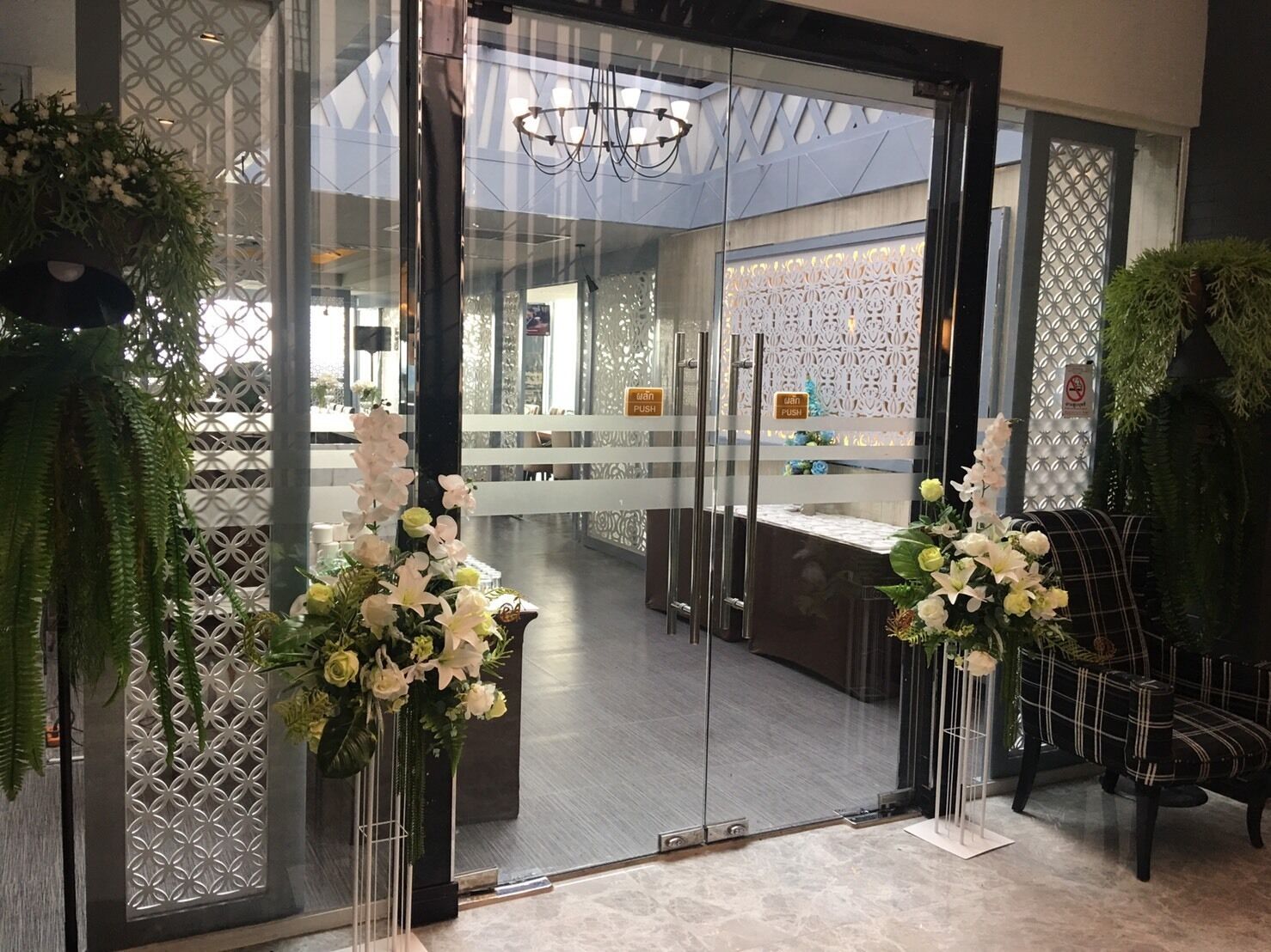 A modern hotel lobby with glass doors, a reception desk, and decorative plants.