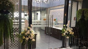 A modern hotel lobby with glass doors, a reception desk, and decorative plants.