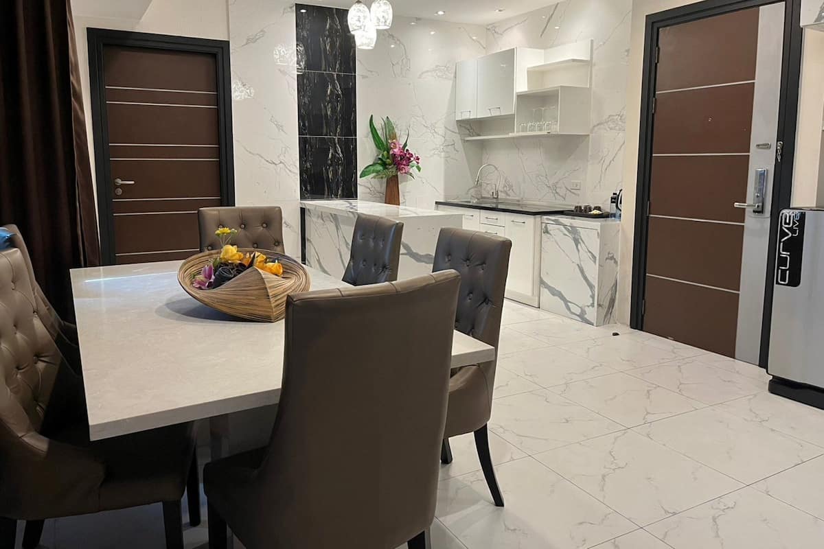 Un comedor moderno con suelo de mármol, una isla central con pileta y una mesa de buffet con flores.