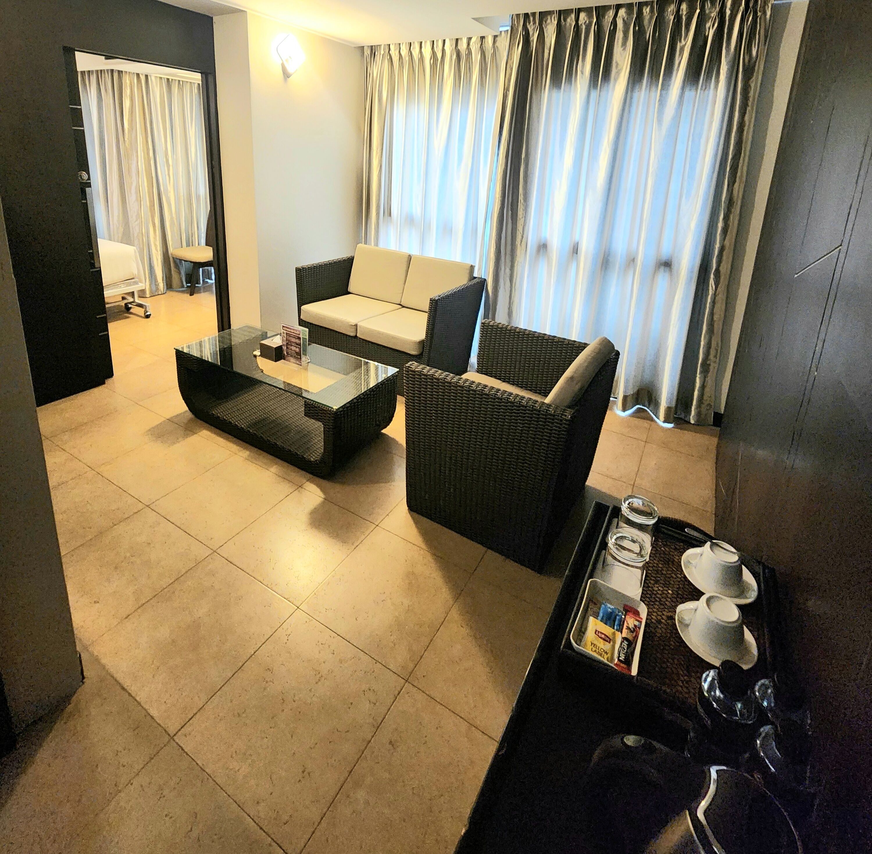 A modern living room with a glass coffee table, a sofa, and a dining area with a tray of tea and snacks.