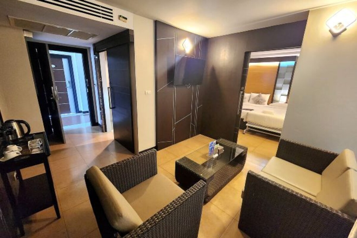 A hotel room with a bed, a TV mounted on the wall, a coffee table, and wicker furniture.