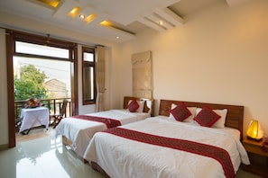 A hotel room with two beds, a balcony with a table and chairs, and a view of greenery outside.