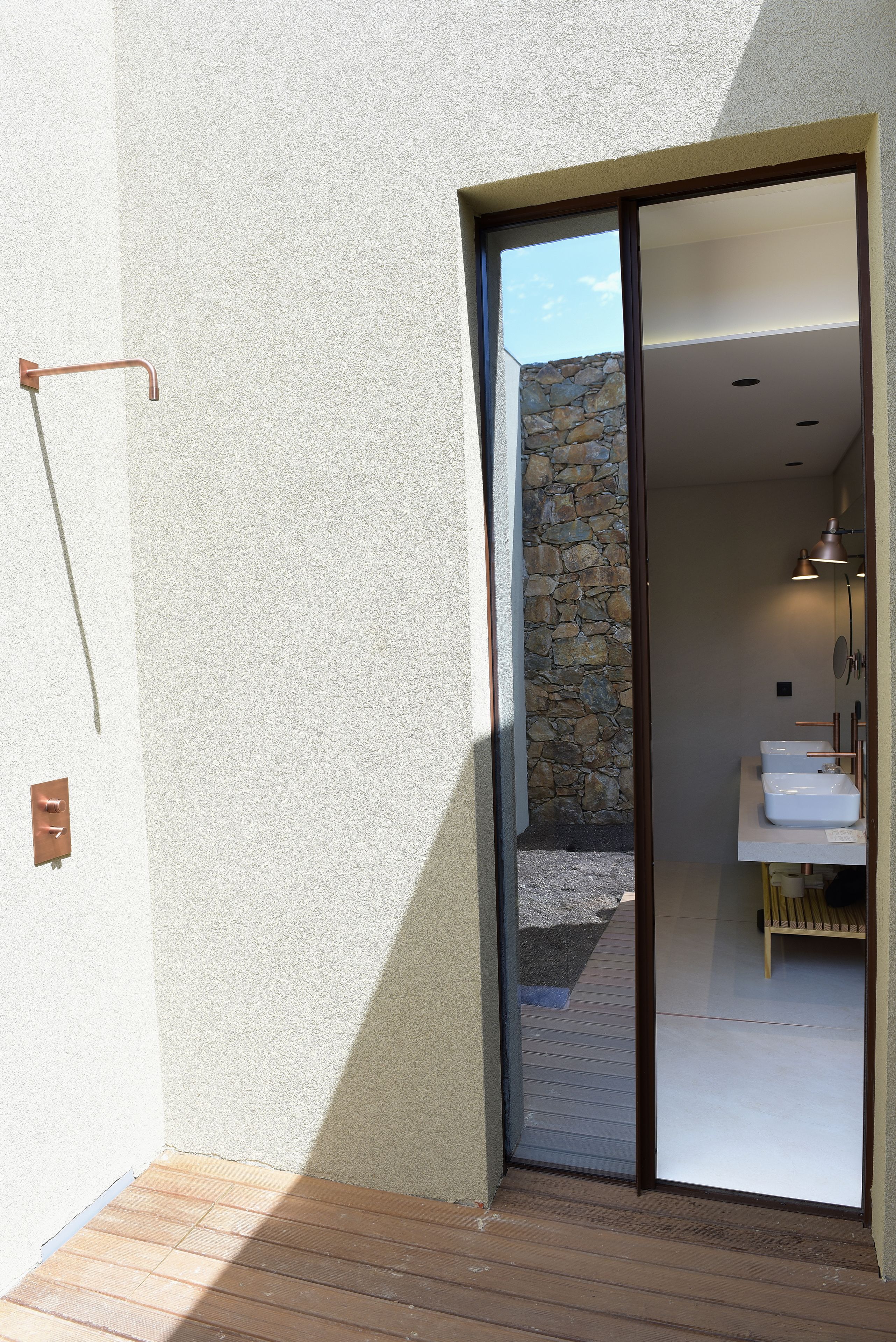 A modern bathroom with a stone wall, a wooden bench, and a large sliding door leading to a balcony.