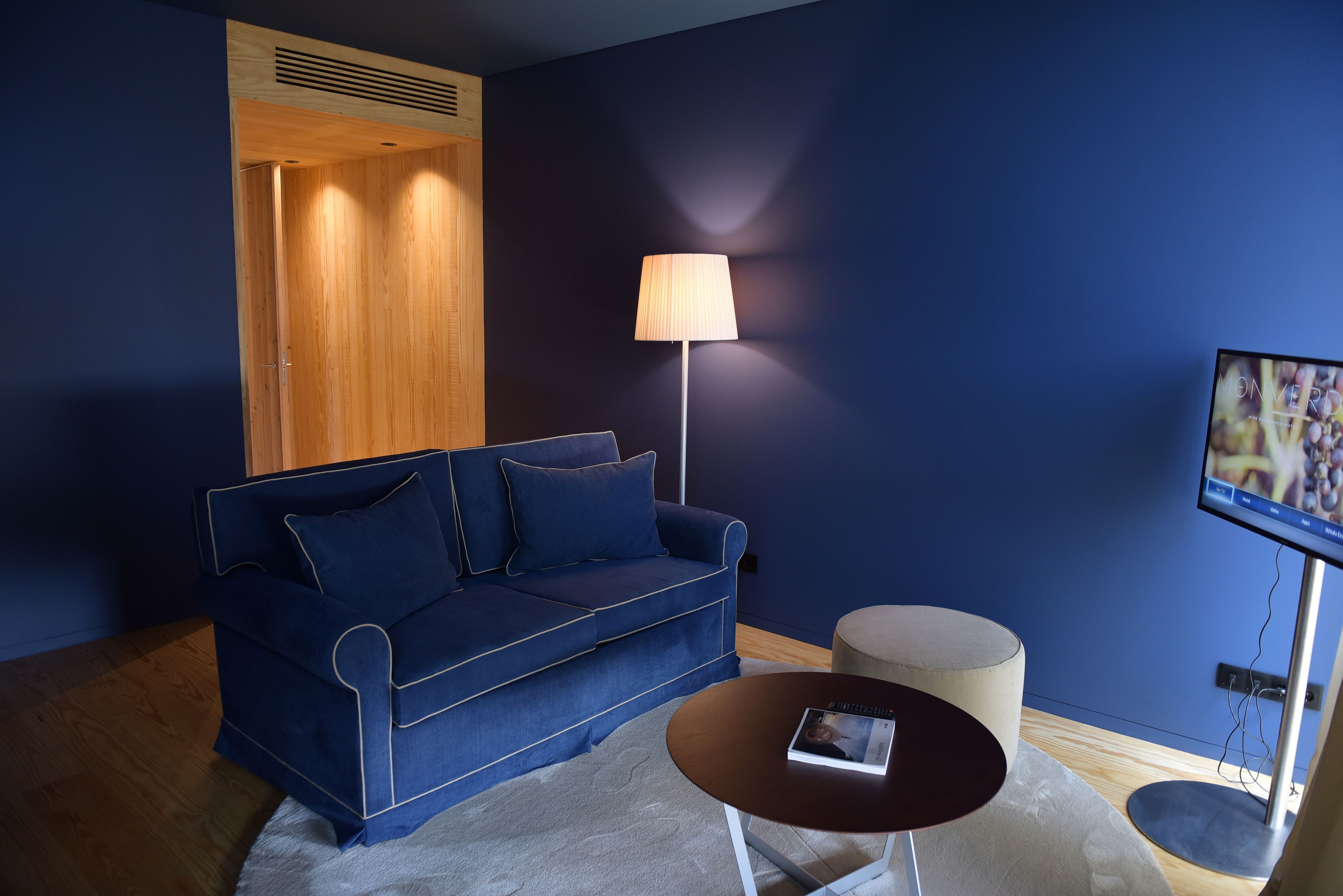 Una sala de estar moderna con un sofá azul, una mesa de centro redonda, una lámpara y un televisor.