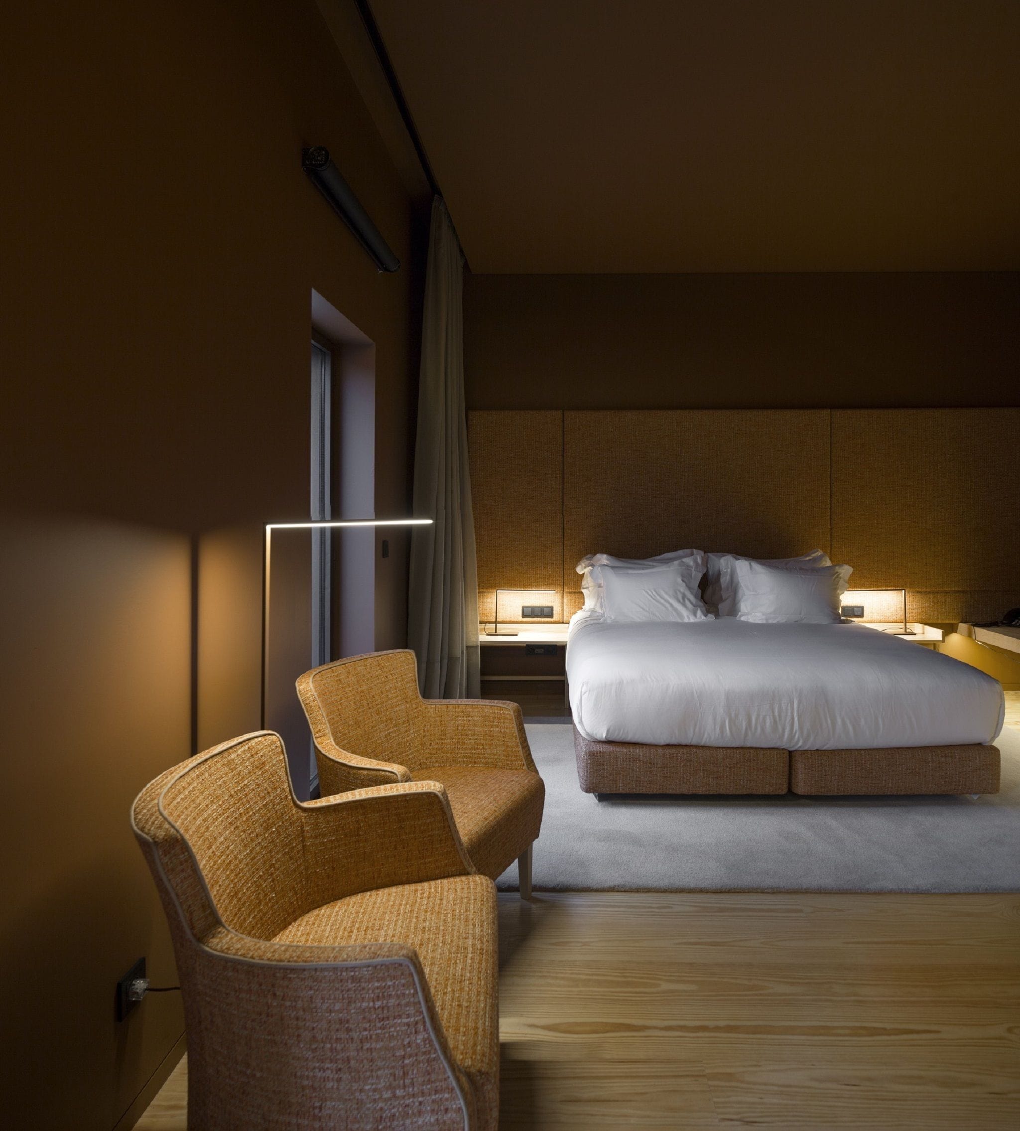 A hotel room with a large bed, two armchairs, a desk, and a bedside table with lamps.