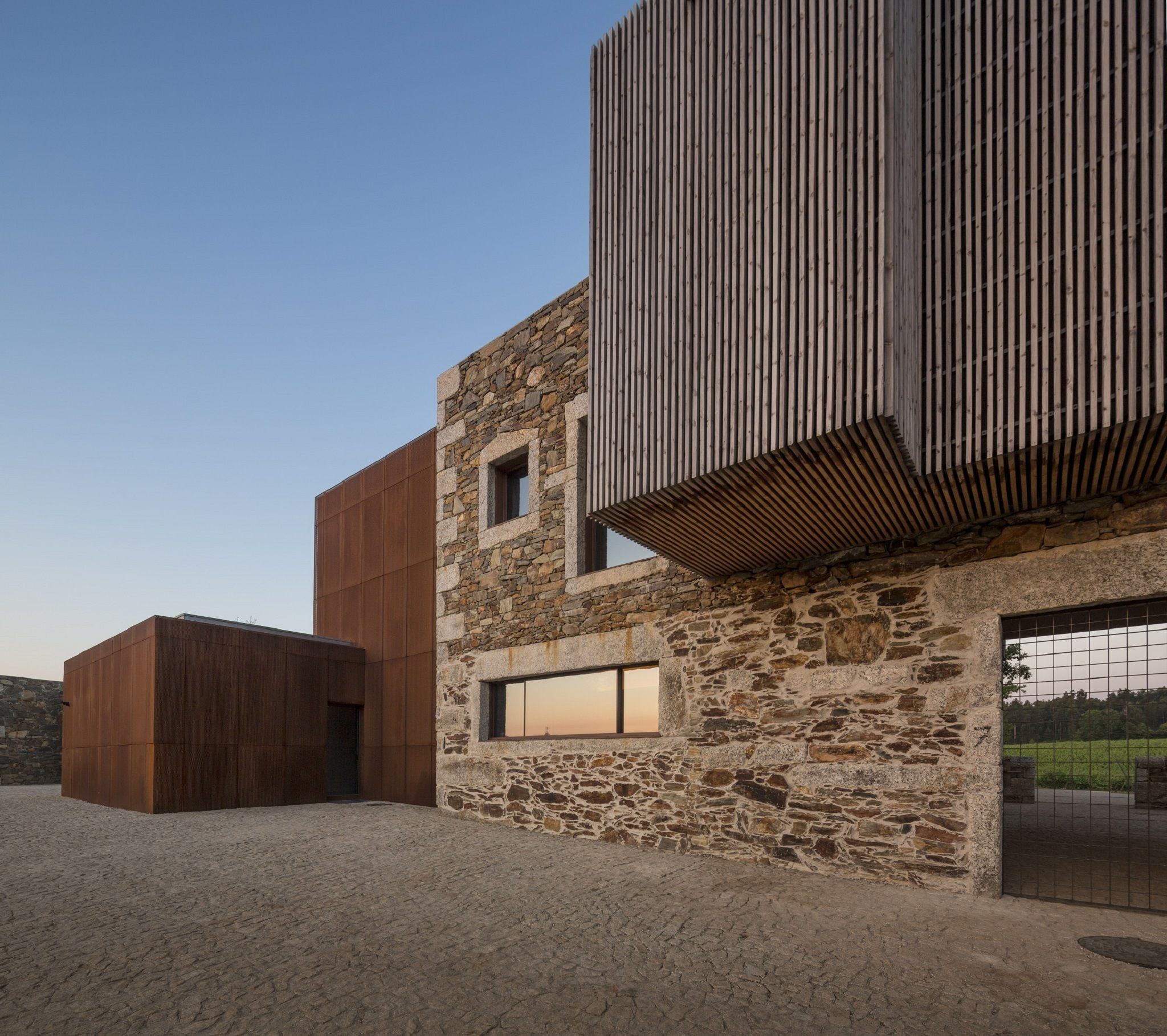 Un edificio moderno con fachada de piedra, un panel de madera grande y una estructura metálica.