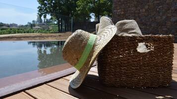 A woven basket with a straw hat on a wooden deck by a pool.