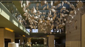 Un vestíbulo espacioso con techo alto, decoraciones colgantes de hojas de madera, asientos verdes y un diseño de interiores moderno.