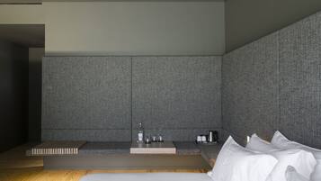 A modern hotel room with a large bed, a small seating area with a table, and a built-in sink.