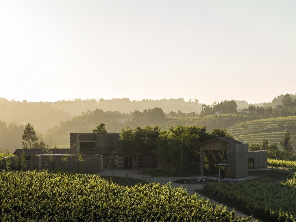 A modern building with a stone facade, surrounded by lush greenery and fields.