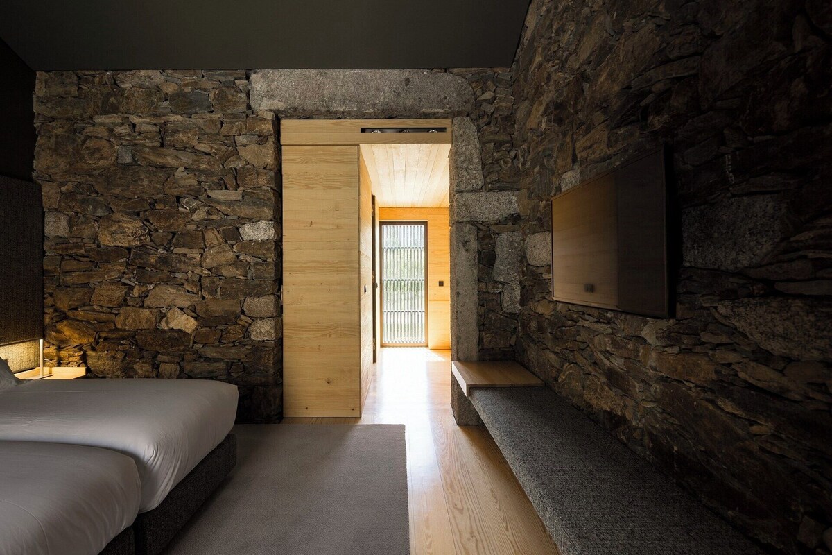 A bedroom with a stone wall, a wooden door, and a bed.