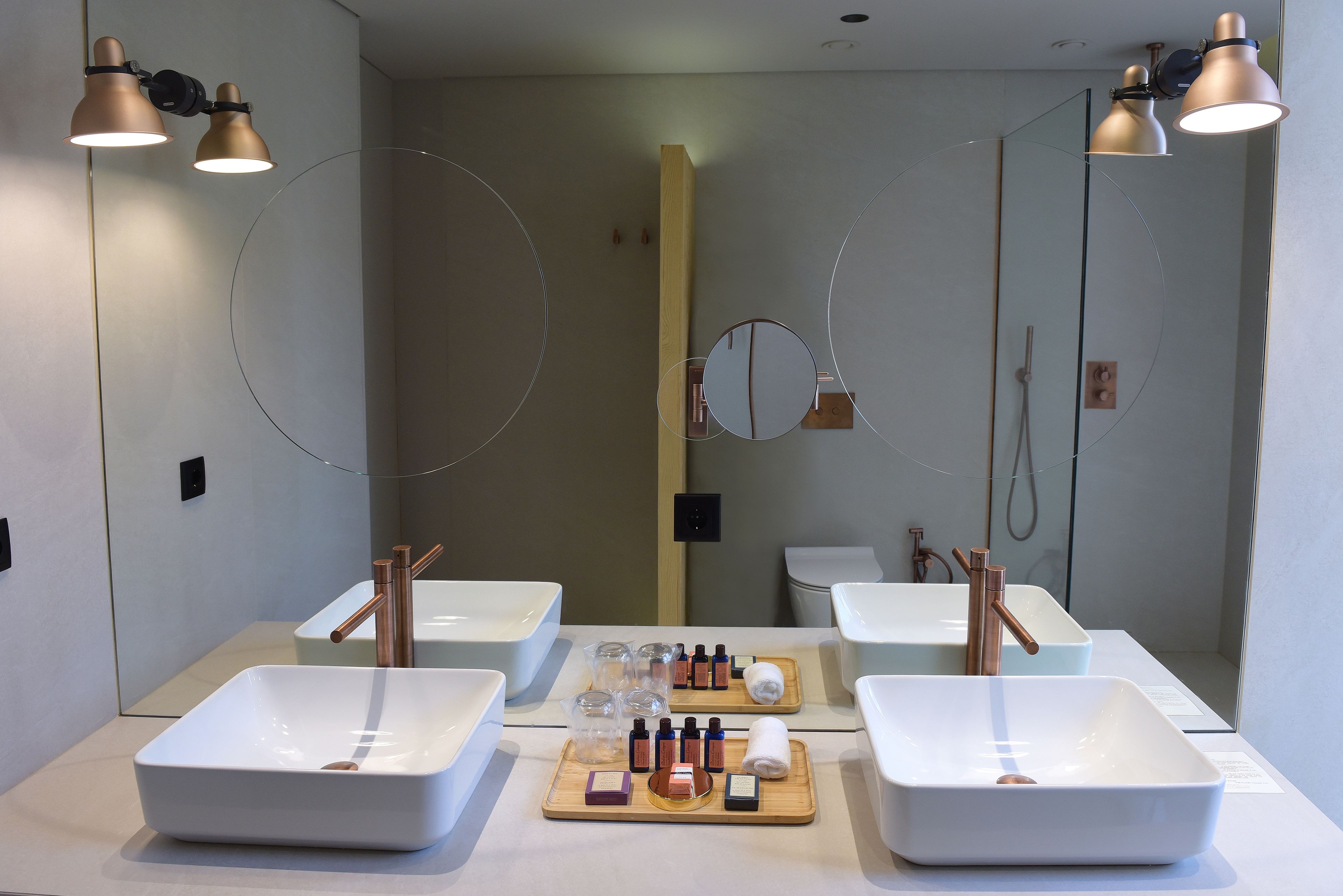 Un baño moderno con dos lavamanos, cada uno con un grifo de cobre, y un espejo encima. Hay artículos de aseo en una bandeja entre los lavamanos.