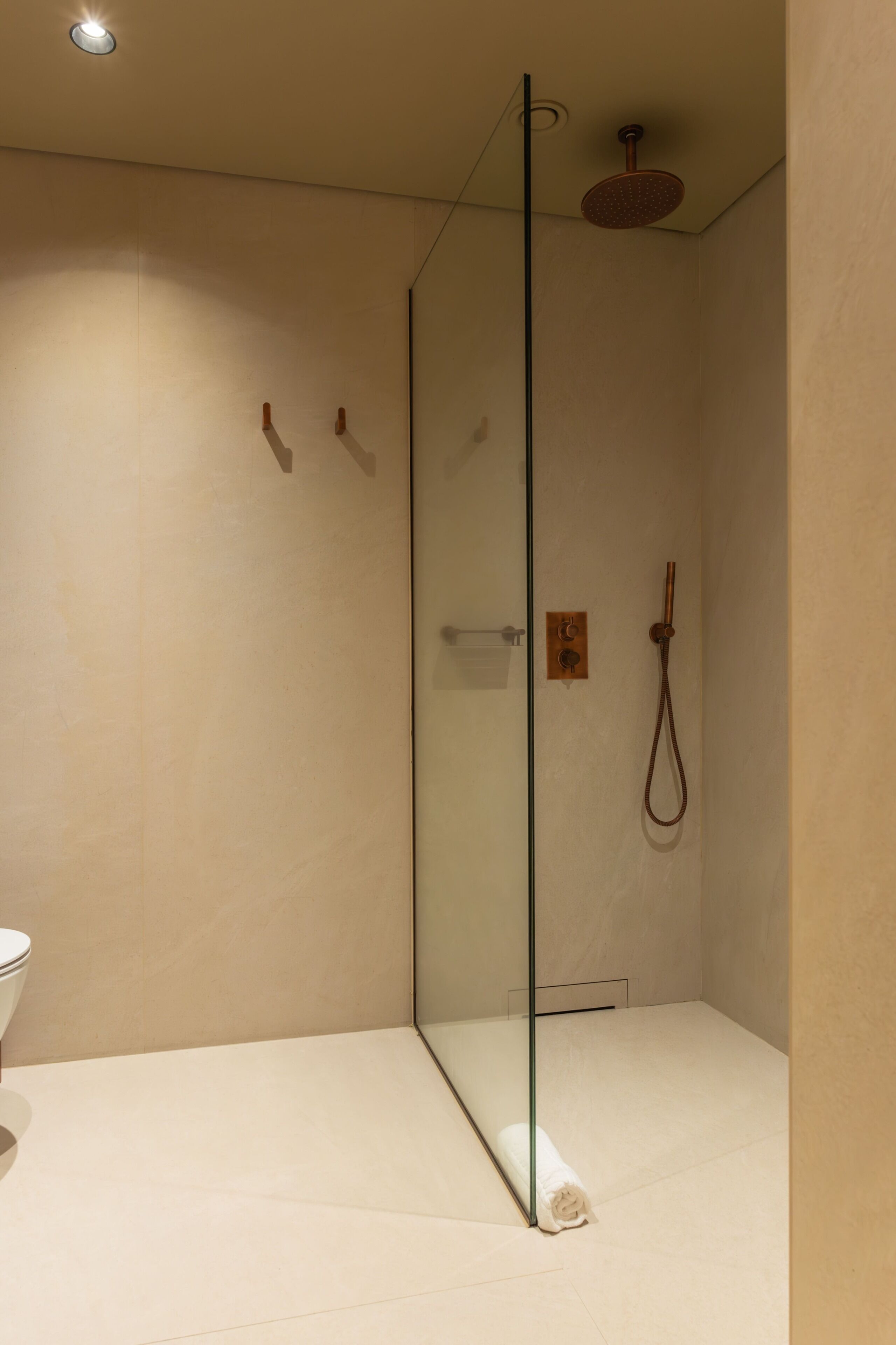 A modern bathroom with a glass-enclosed shower, a toilet, and a towel on the floor.