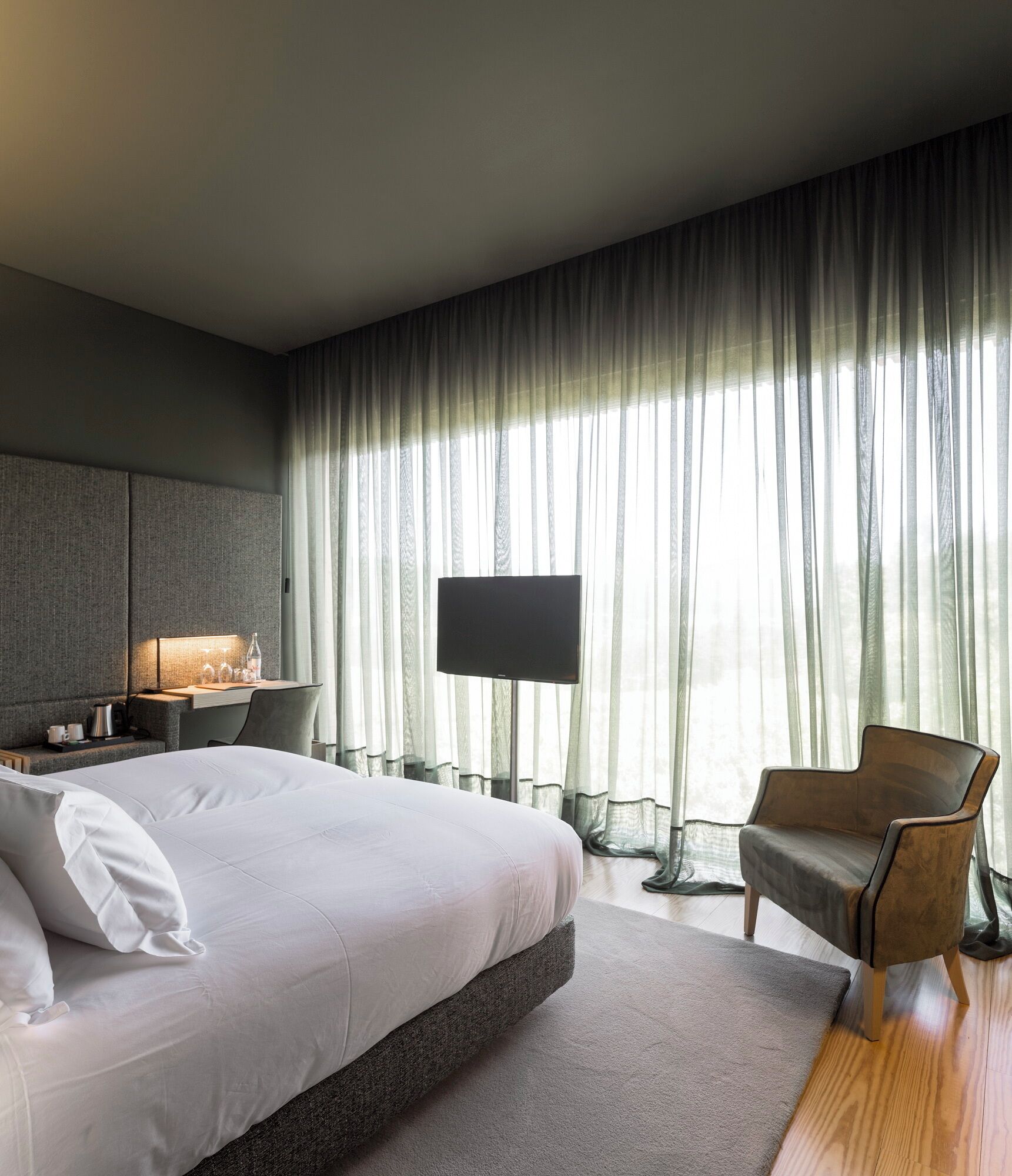 A modern bedroom with a large bed, a bedside table with a lamp, a chair, and a TV.
