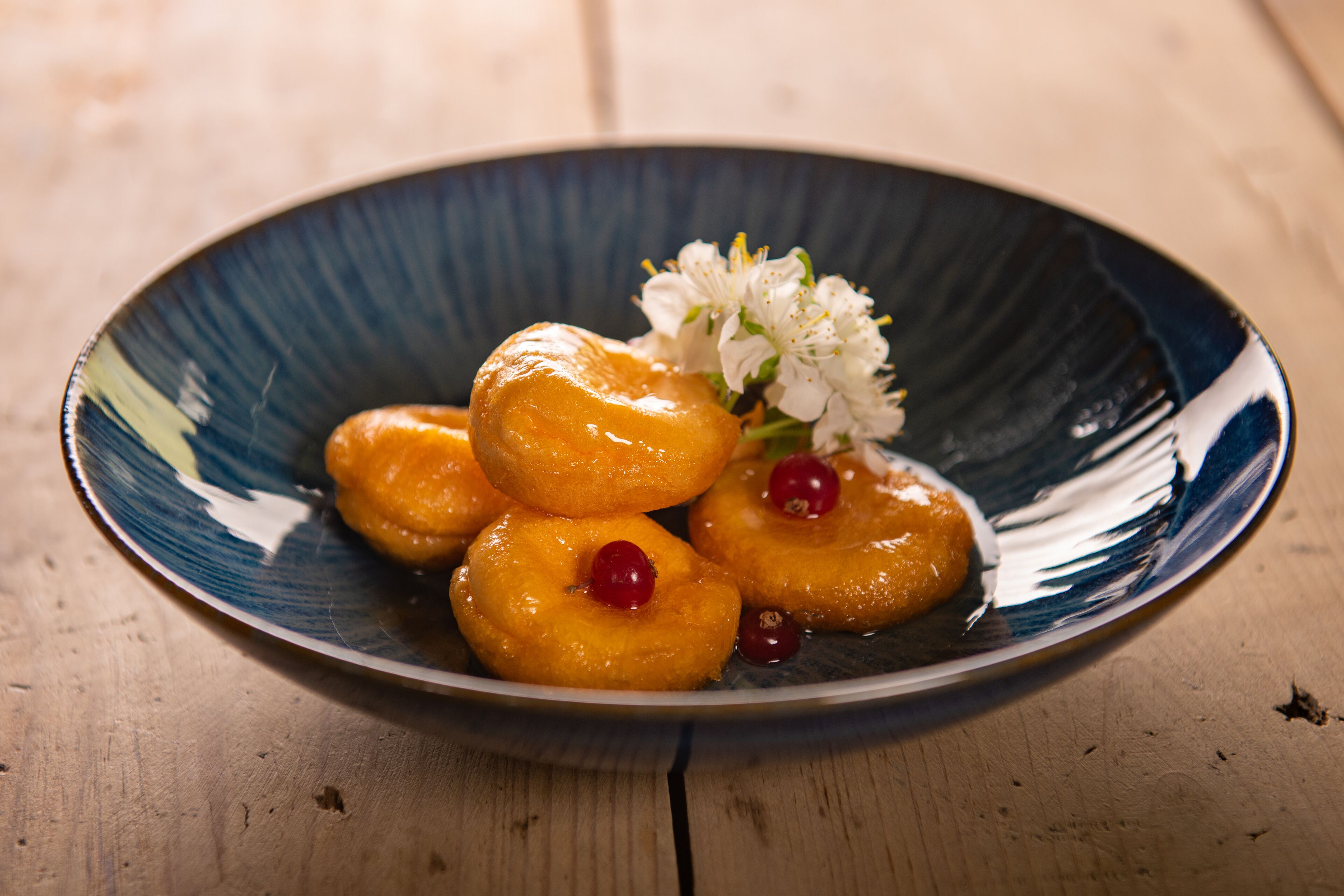 A plate of glazed donuts with cherries on a wooden table.