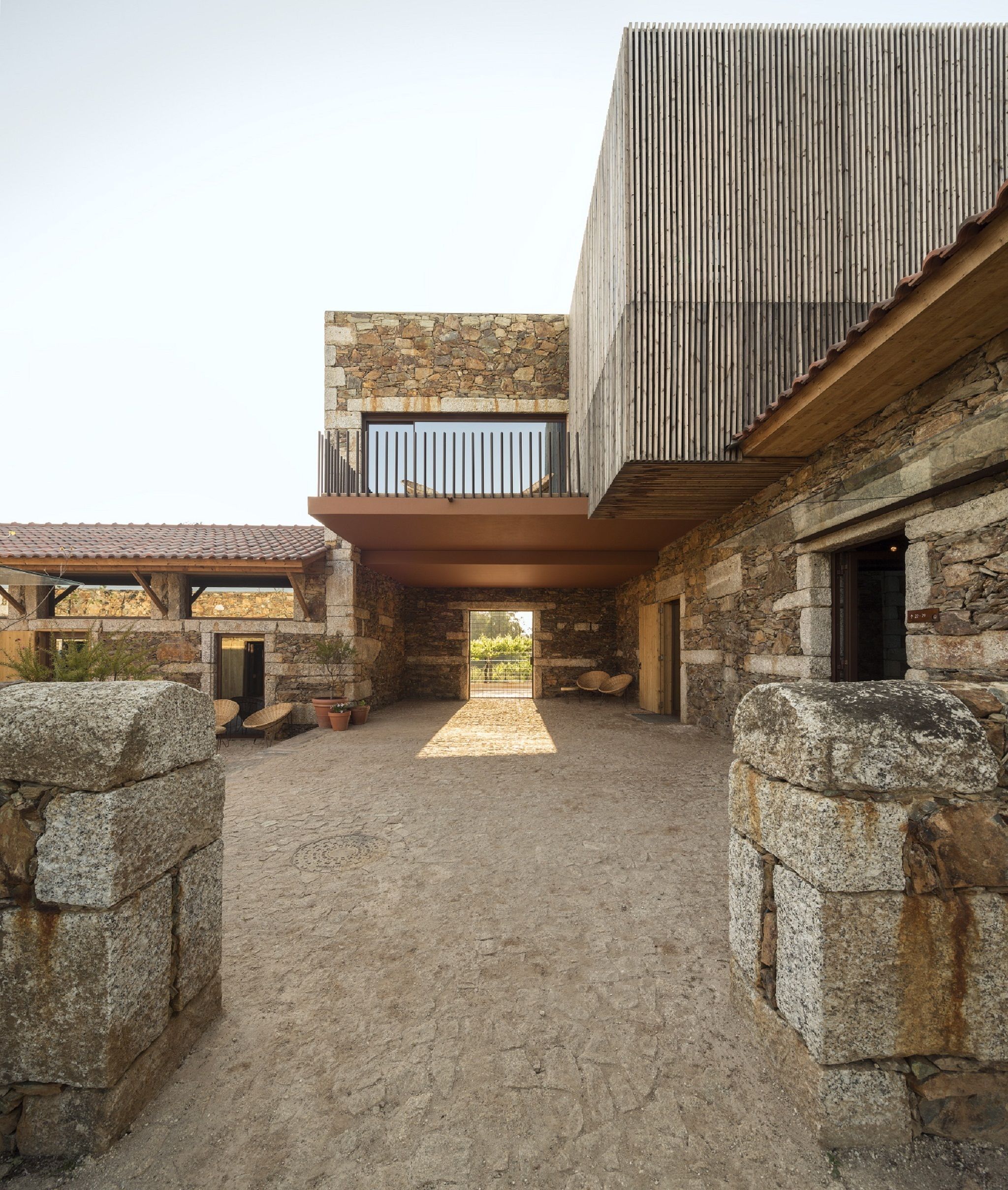A courtyard with a stone pathway leading to a building with a wooden deck and stone walls.