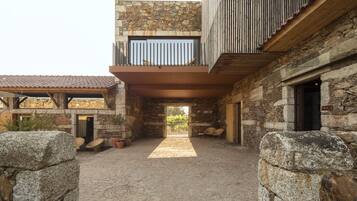 A courtyard with a stone pathway leading to a building with a wooden deck and stone walls.