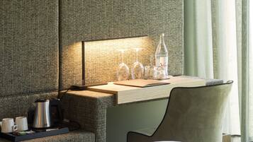 A hotel room with a bed, a desk with a lamp, a coffee maker, and a bottle of water.