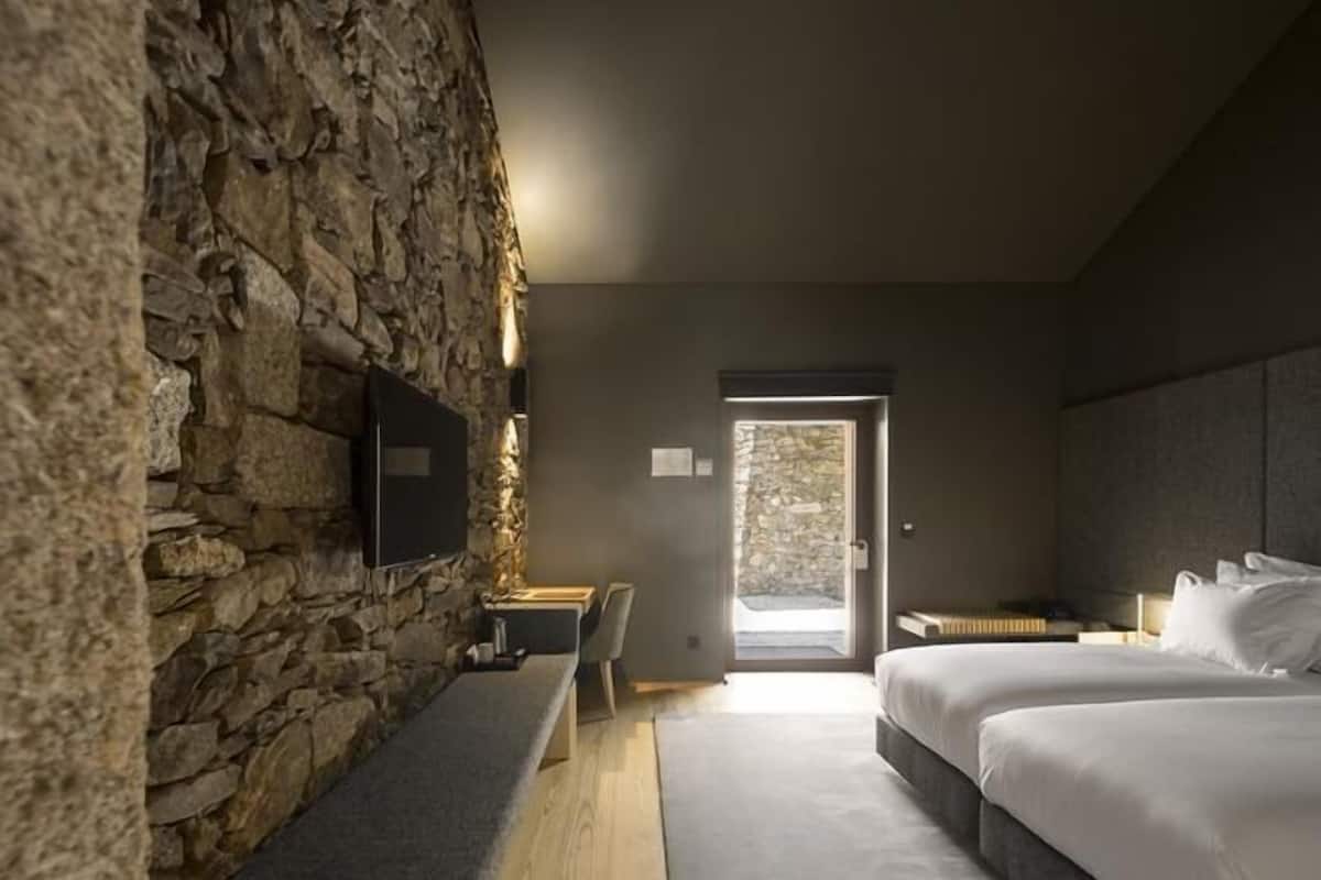 A modern bedroom with a stone wall, a wooden bench, a bed, and a TV.