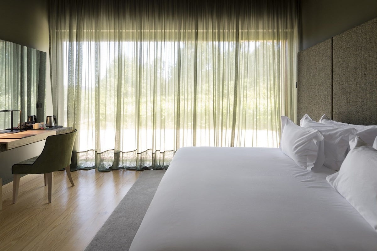 A modern hotel room with a large bed, a desk, and a chair.
