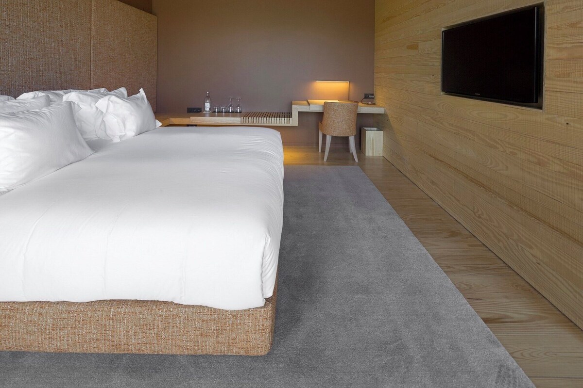 A modern hotel room with a large bed, a desk with a flat-screen TV, and a seating area with a chair.