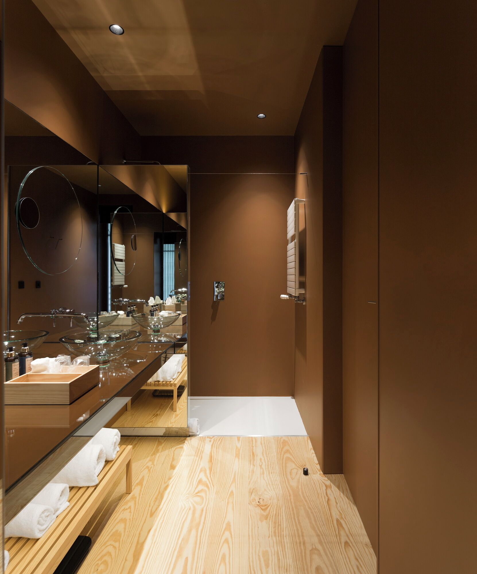 A modern bathroom with a large mirror, glass bowl sinks, and wooden flooring.