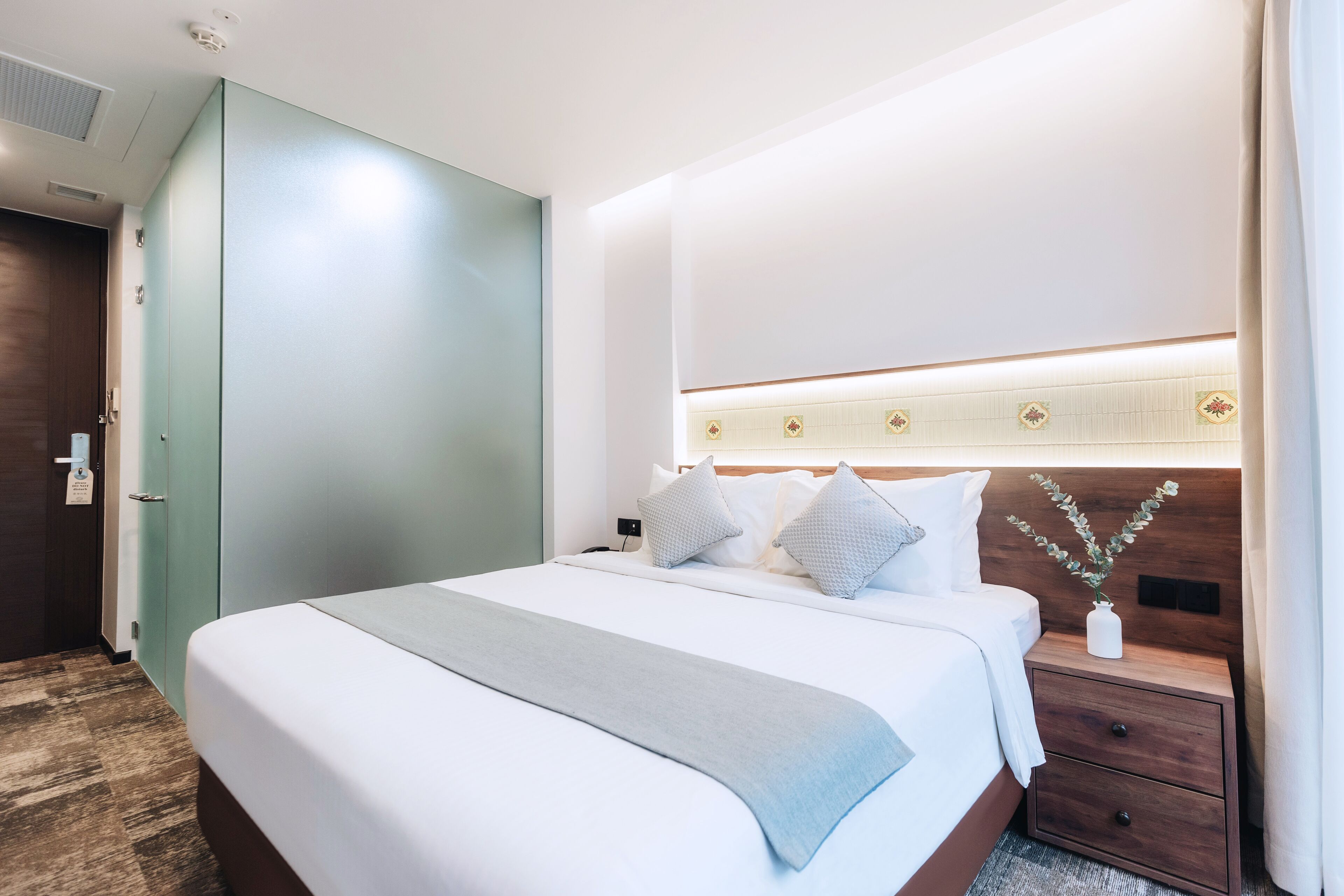 Une chambre d’hôtel avec un grand lit, une table de chevet, une lampe de chevet, une tête de lit en bois et un luminaire fixé au mur.