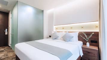 Une chambre d’hôtel avec un grand lit, une table de chevet, une lampe de chevet, une tête de lit en bois et un luminaire fixé au mur.
