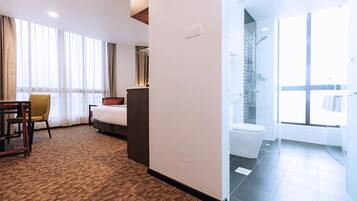 A hotel room with a bed, a desk, a chair, a bathroom with a toilet and shower.