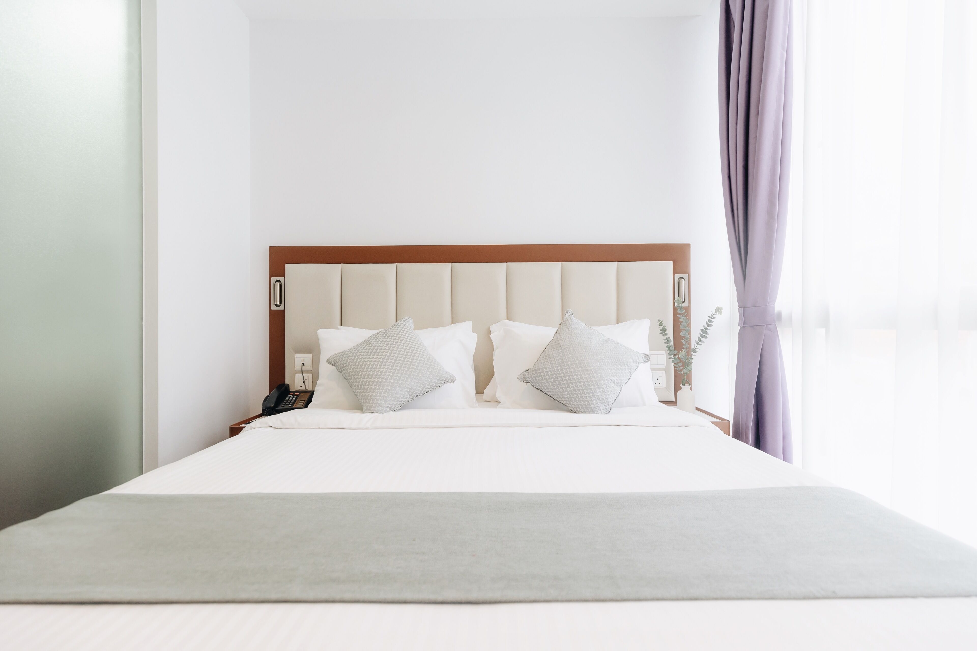 A neatly made bed with a wooden headboard, white bedding, and two pillows.