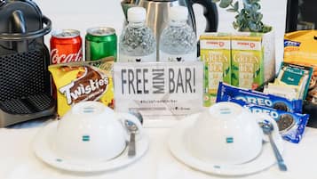 A breakfast setup with a Nespresso machine, two cups, a sign reading "FREE MINI BAR", and various snacks and drinks.