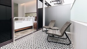 A modern hotel room with a bed, a chair, and a patterned floor.