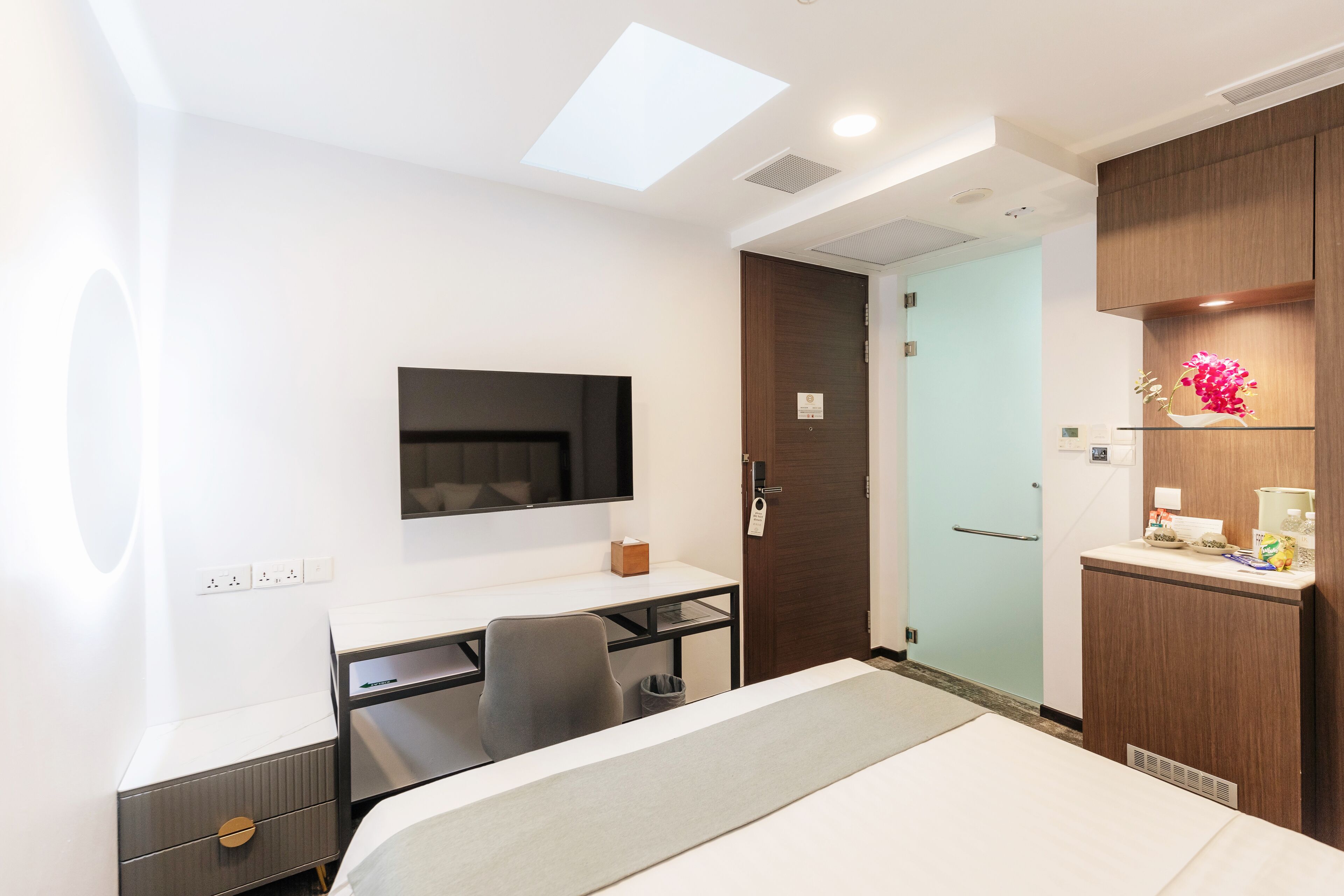 Habitación de hotel con cama, escritorio, silla, televisor, armario y puerta de baño.