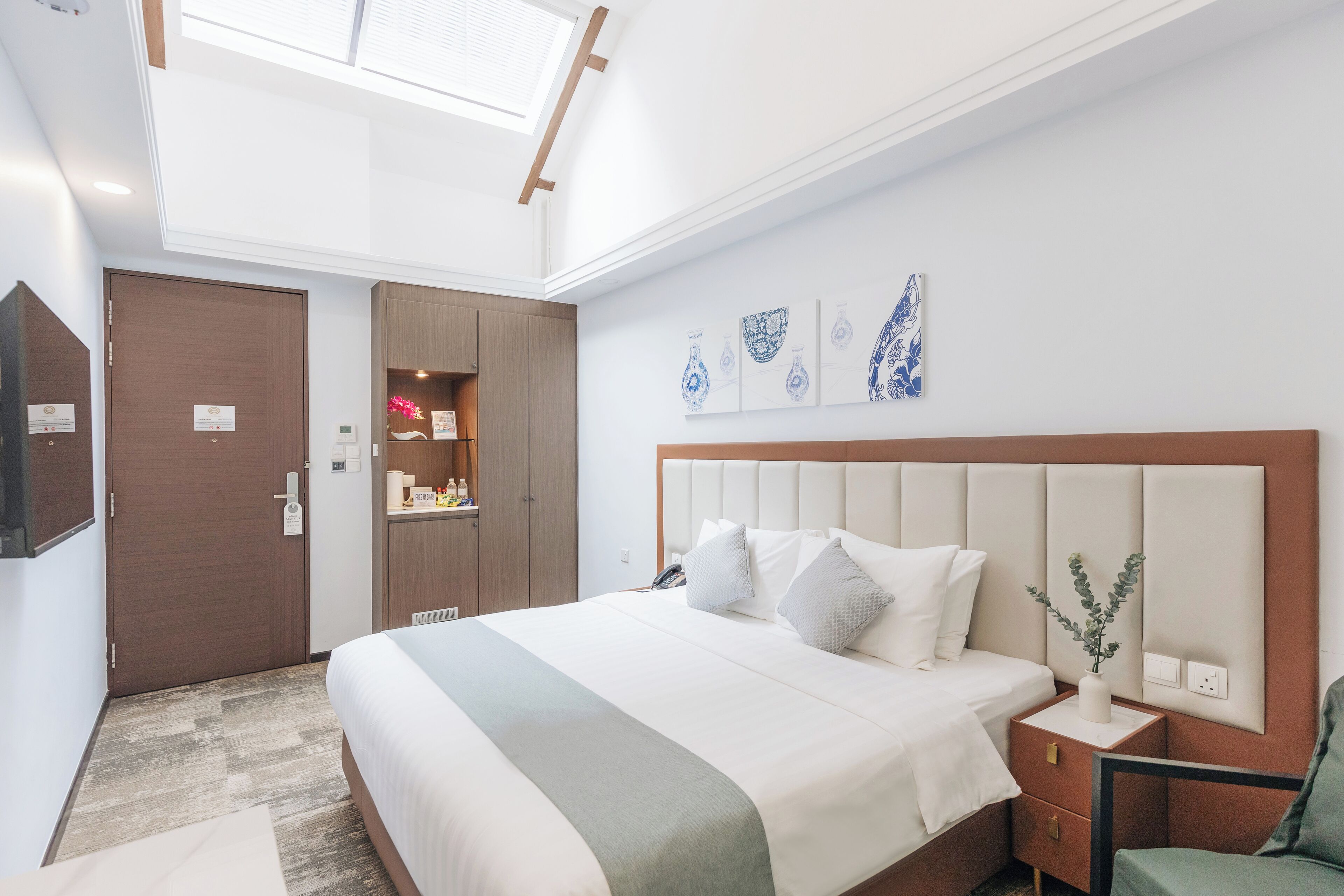 Een hotelkamer met een groot bed, een nachtkastje met een vaas, en kunst aan de muur.
