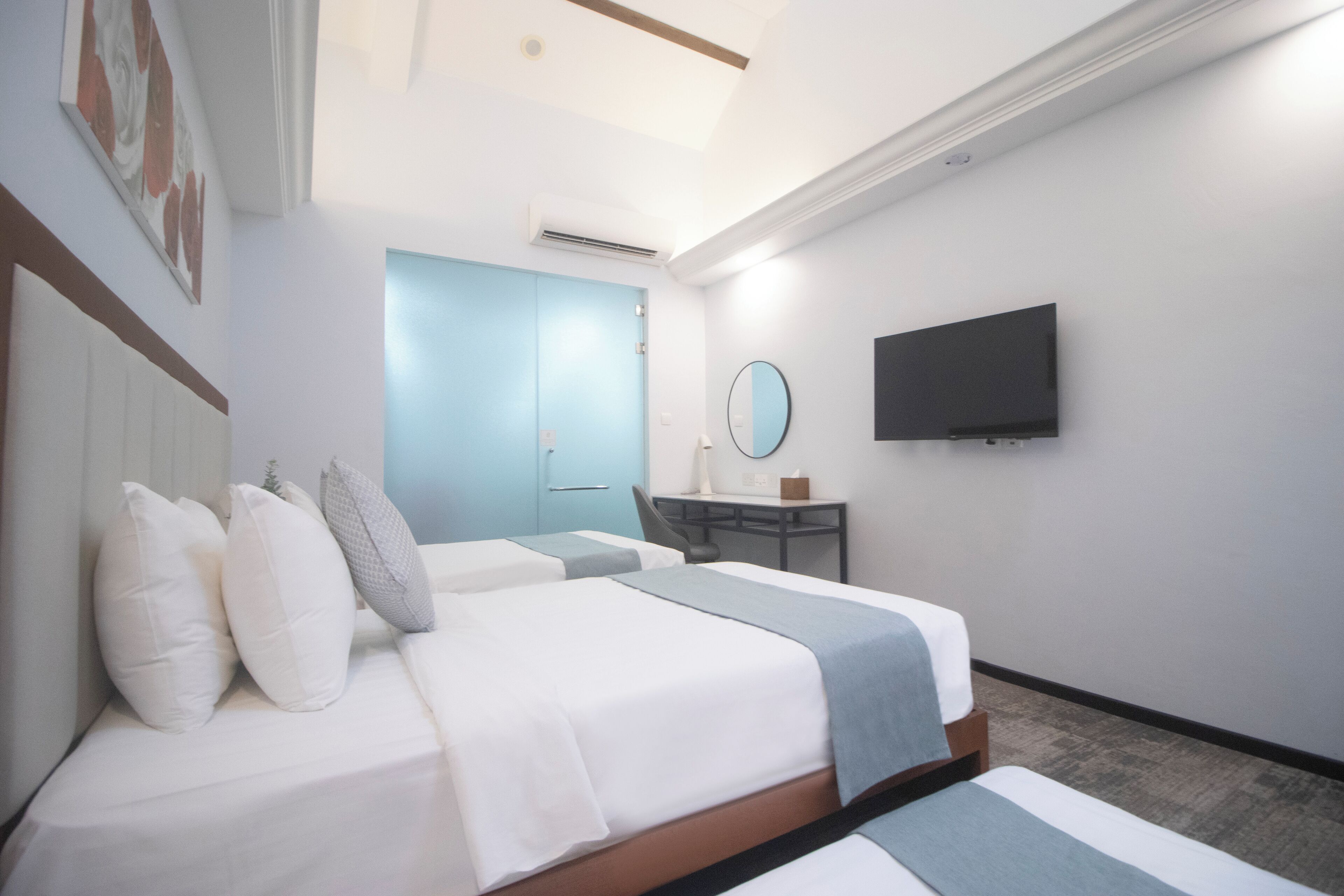 Une chambre d’hôtel avec deux lits, un bureau, une chaise, une télévision et une salle de bain avec une porte bleue.