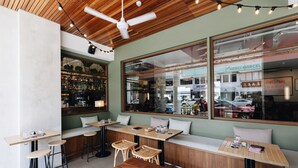 A modern cafe with wooden tables and chairs, large windows, and a view of the street outside.