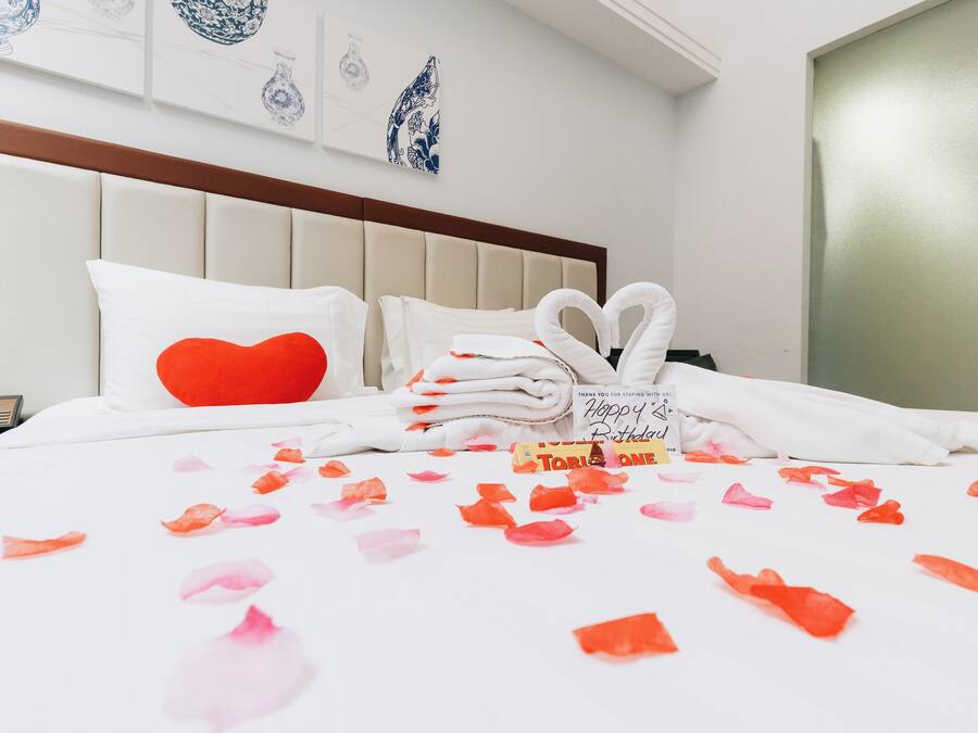 A neatly made bed with a red heart pillow, white towels, and a thank you card.