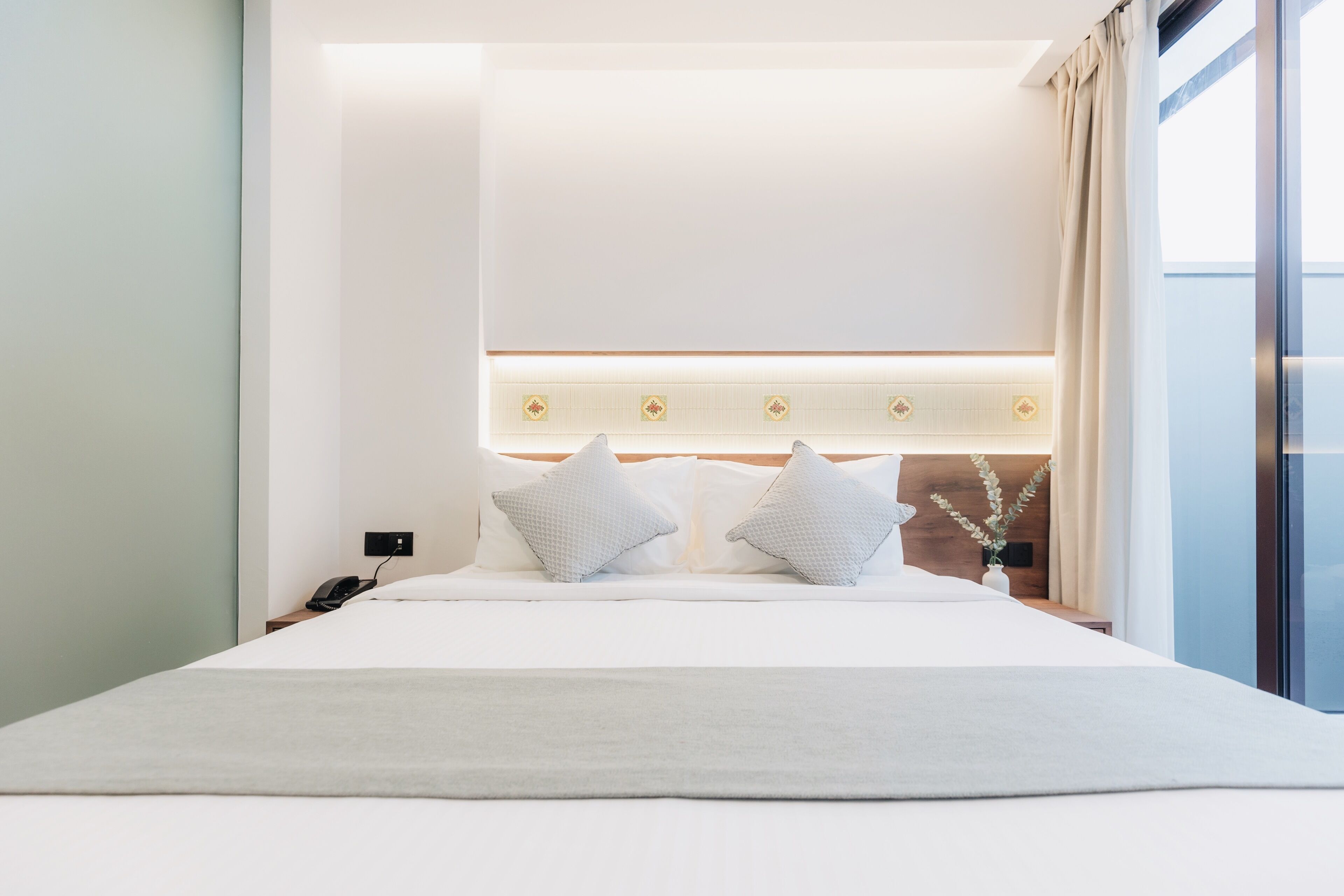 Una habitación de hotel moderna con una cama grande, una mesita de noche con teléfono y vistas al exterior.