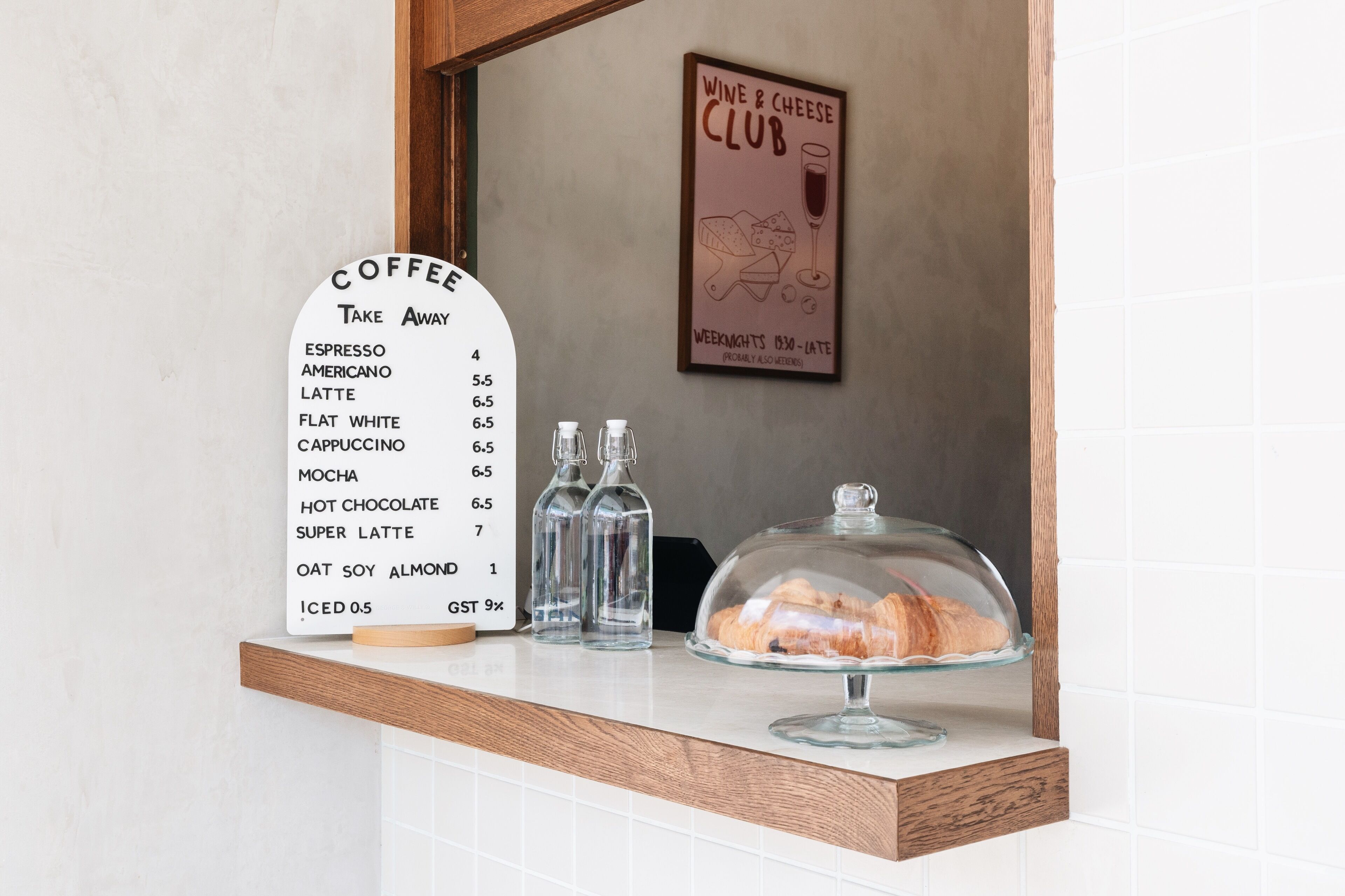 A coffee menu on a counter with a glass display case containing pastries.
